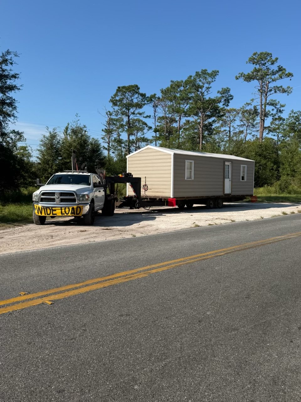Panhandle Shed Haulers truck with a wide load sign hauling a portable building on a gooseneck trailer